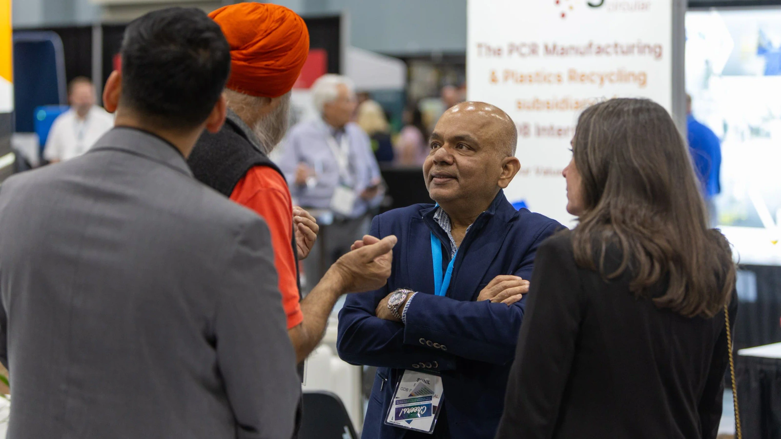 Plastics recycling professionals talk beside an exhibitor booth on the conference floor.