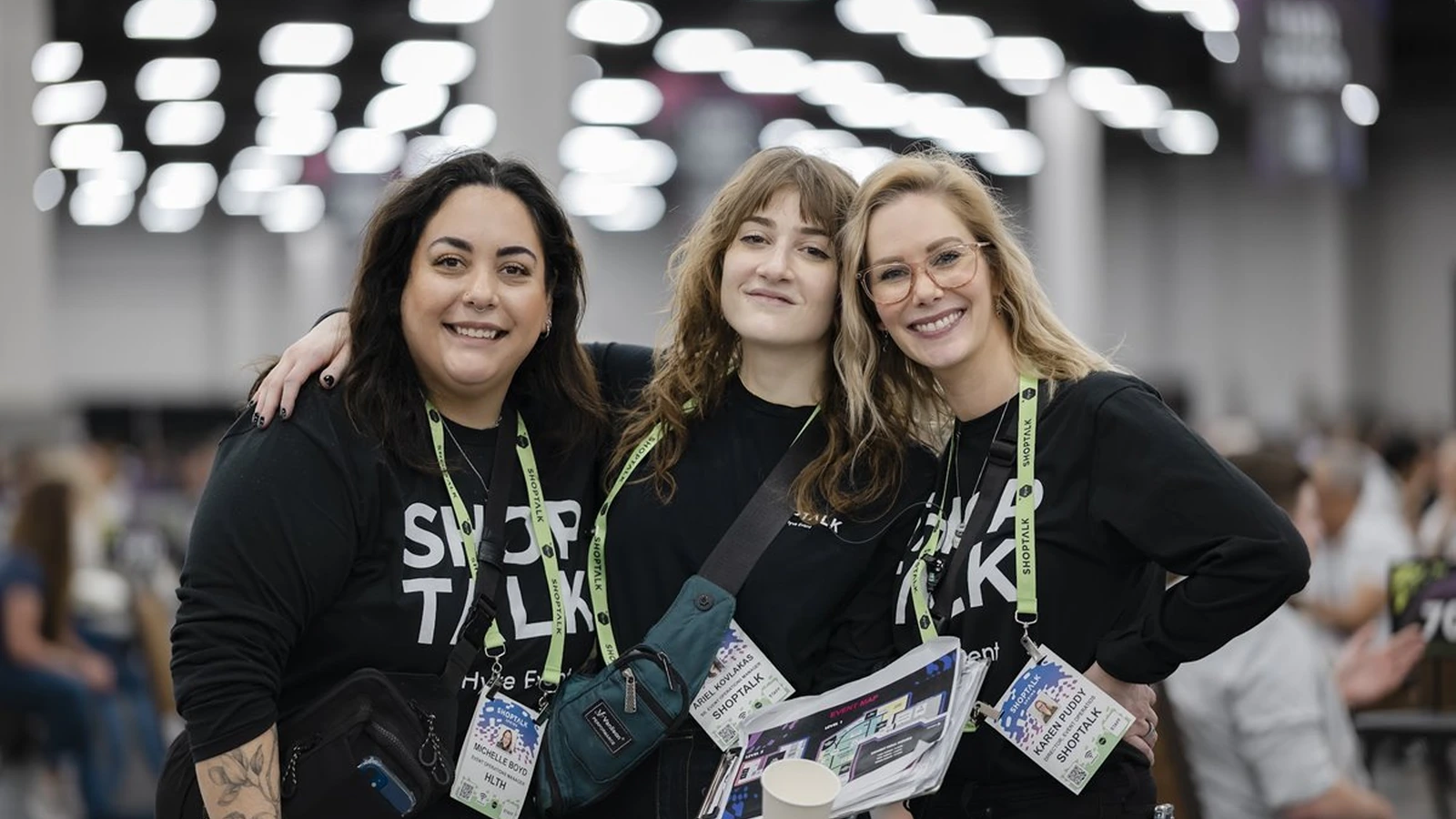 Three attendees wearing Shoptalk shirts pose on the show floor.
