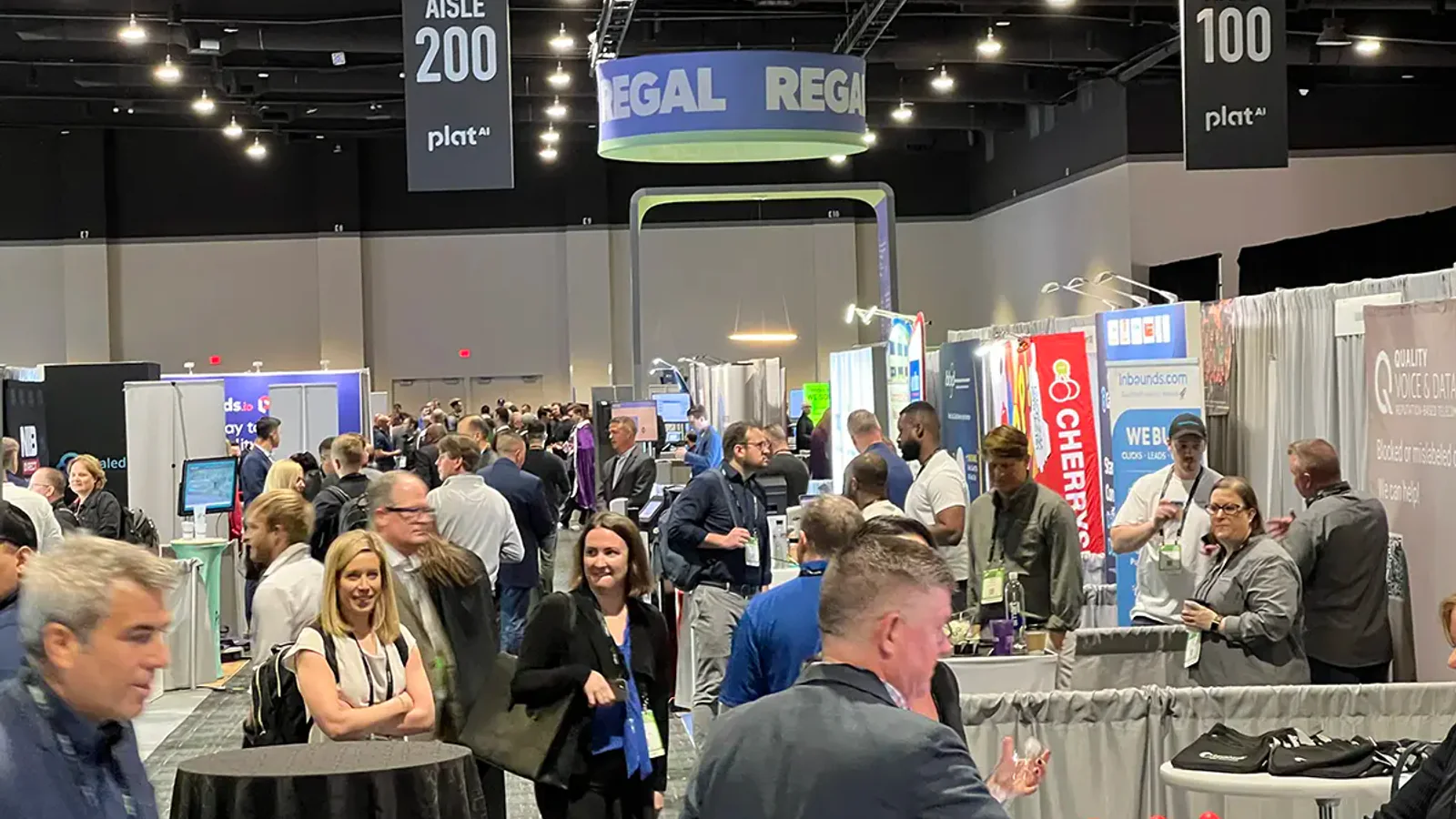 Attendees walk a busy LeadsCon Las Vegas exhibit hall beneath aisle signs.