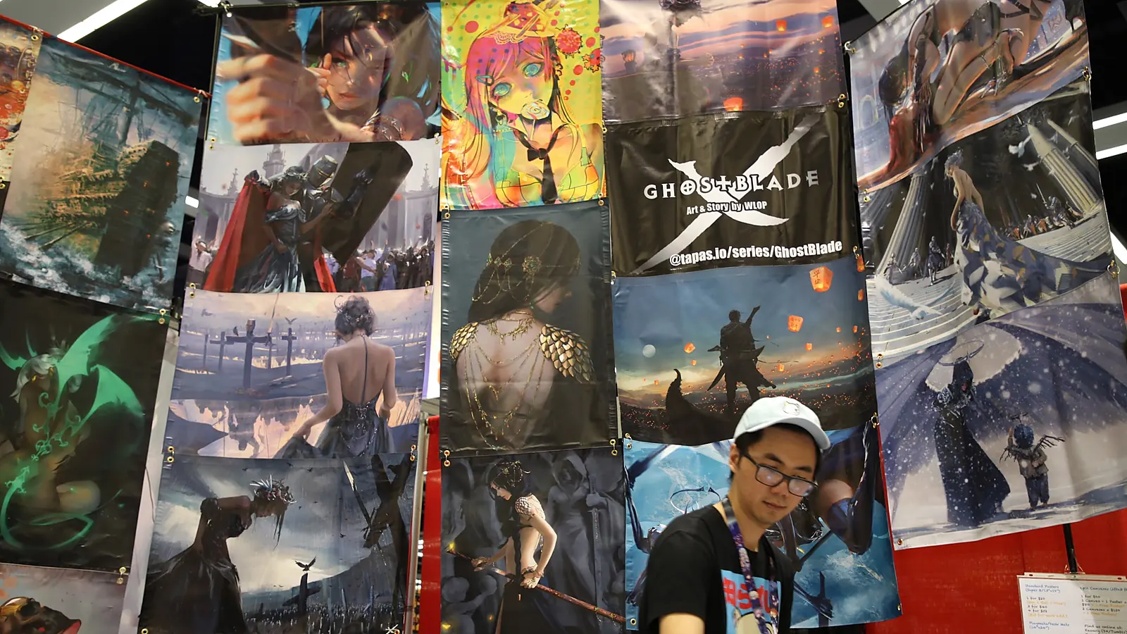 An exhibitor stands beside anime artwork inside a Sakura-Con exhibit hall in Seattle.