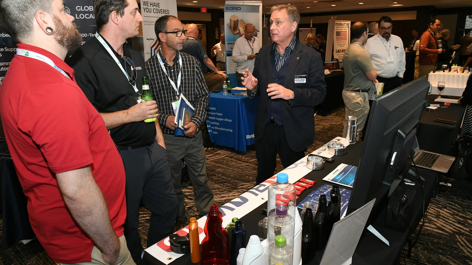 Attendees discuss bottle samples on the 2025 Annual Blow Molding Conference exhibit floor.