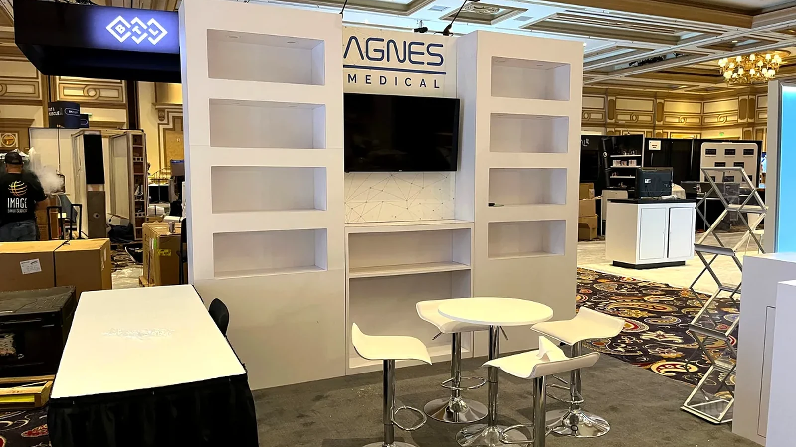 Agnes Medical 10x10 booth with built-in display shelves, a screen and seated conversation furniture.