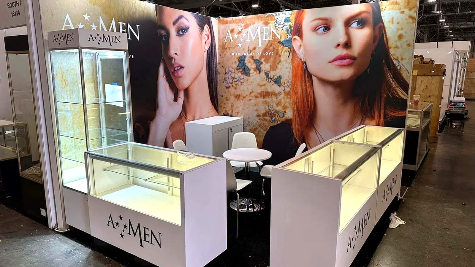 AMEN 10x10 booth with illuminated jewelry showcases and a compact internal meeting area.