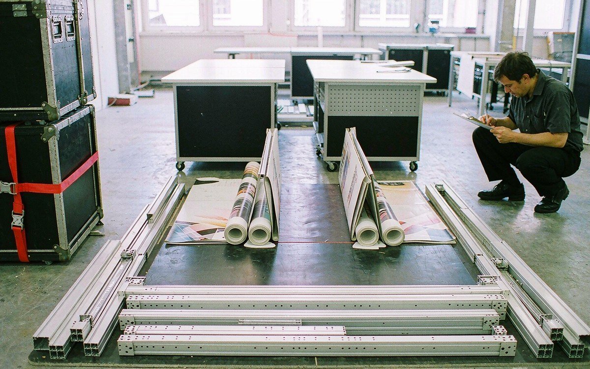 rental corner-exhibit kit laid out on a workshop floor before assembly - flat-pack aluminium frame profiles