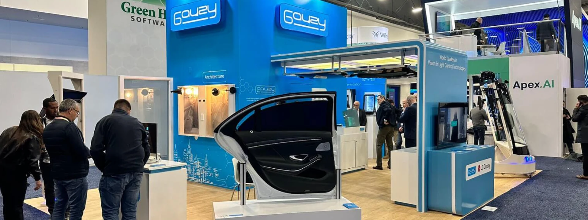 Completed Gauzy island exhibit with blue illuminated structures, automotive glass displays, counters, and visitor space.