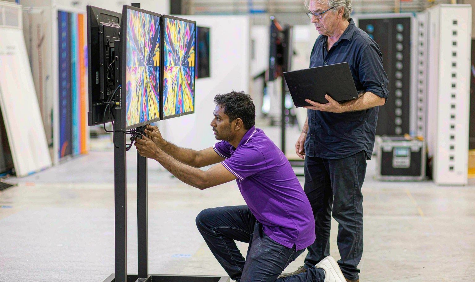 AV technician testing dual screens on a monitor stand during booth pre-build