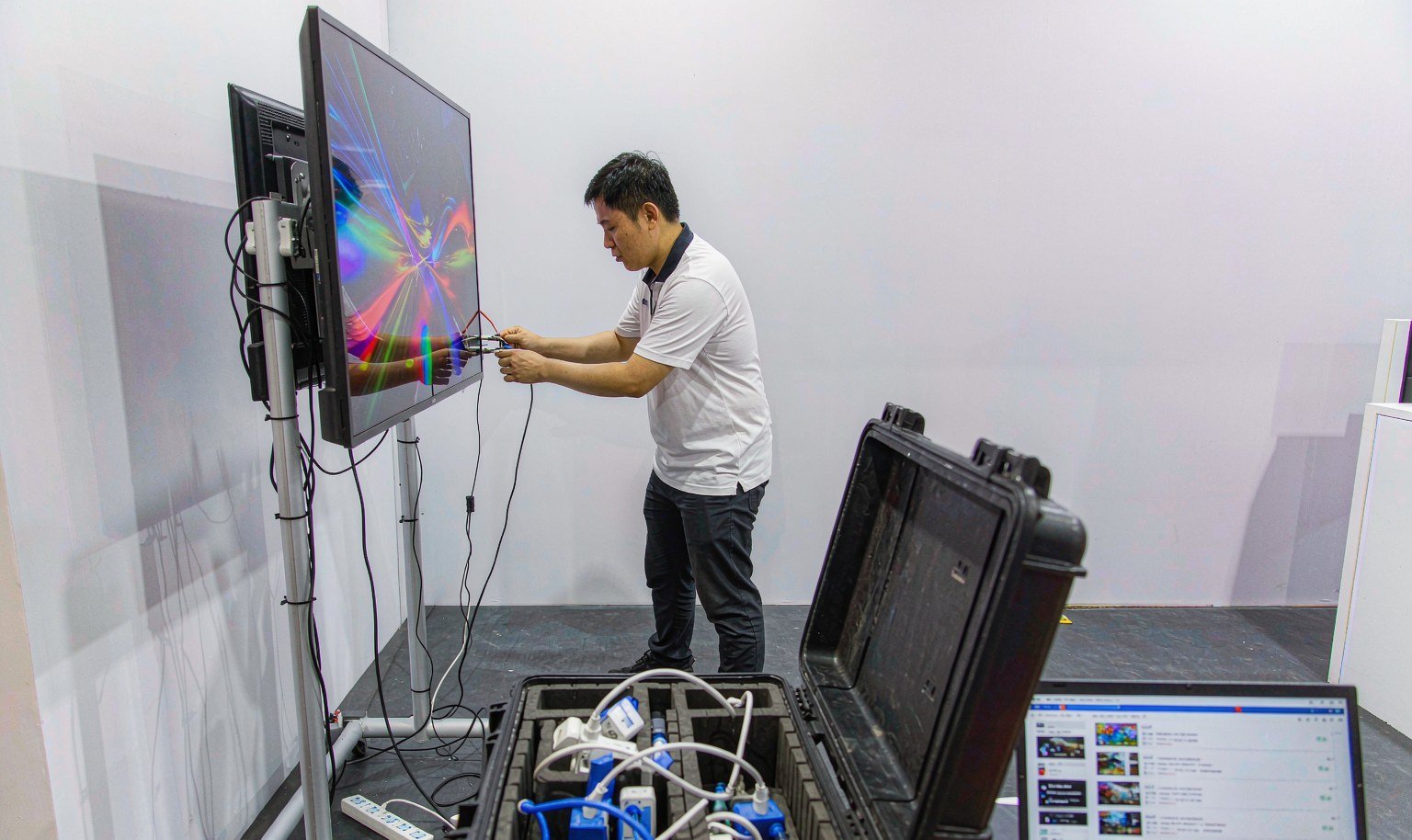 AV technician connects cables and a media player to a monitor stand inside an exhibition booth