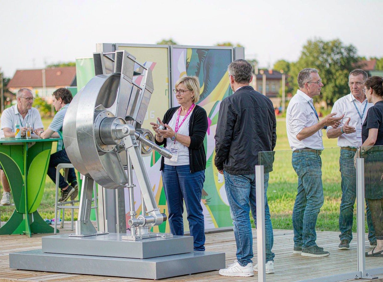 Presenter demonstrating a product at an outdoor booth while visitors watch and others talk nearby