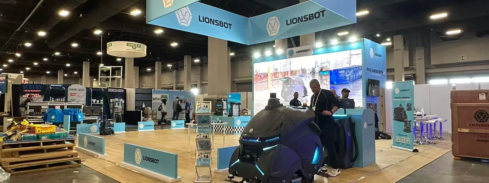 Completed LionsBot island exhibit with an overhead sign, demonstration robots, illuminated counters, and a wood-look platform.