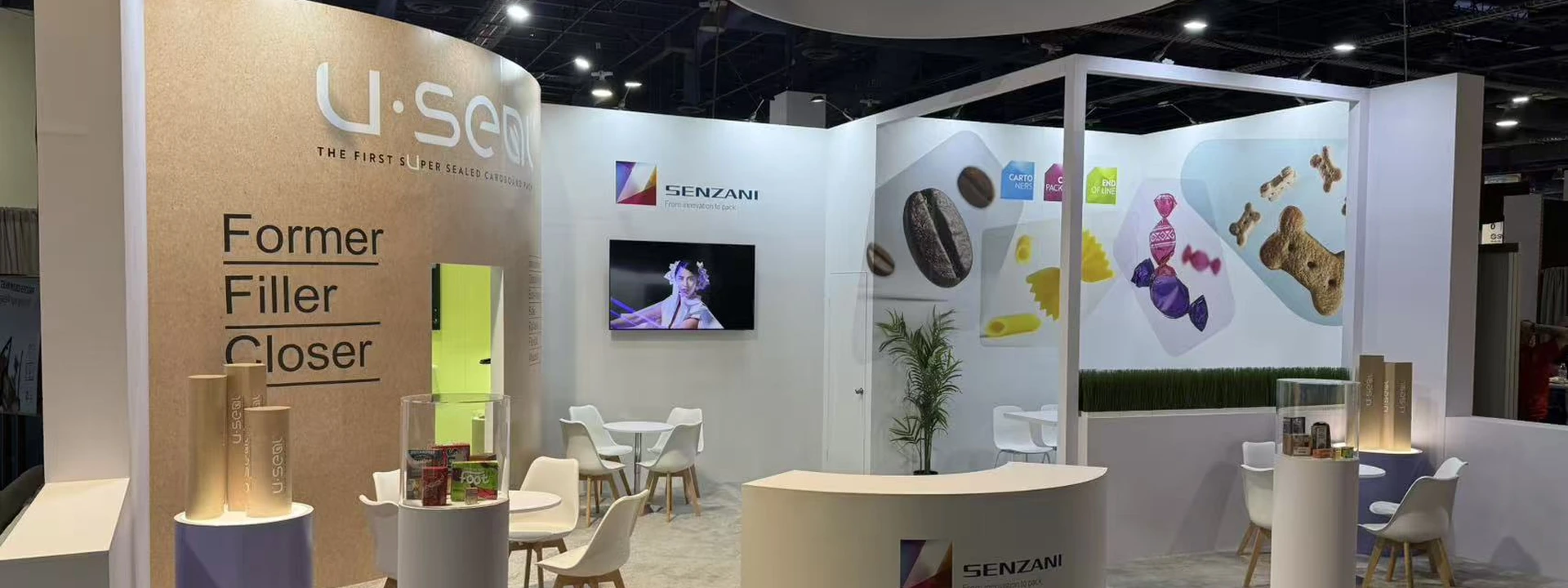 Open trade show booth with a circular hanging sign, curved reception counter, product pedestals, and meeting chairs.