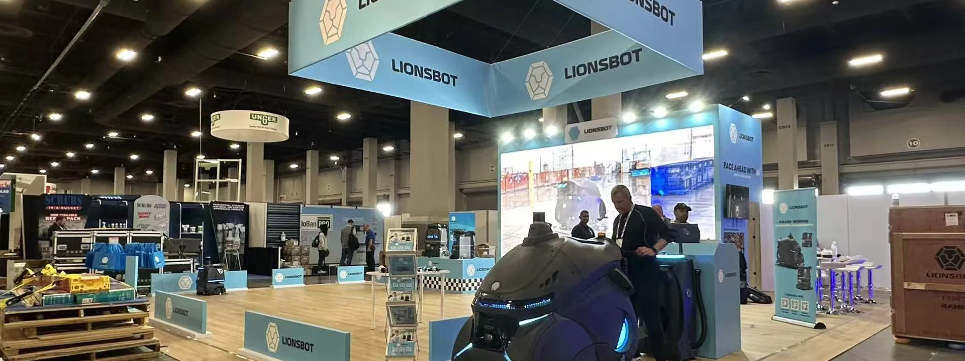 Large island trade show booth with an overhead sign, wood-look platform, counters, and equipment displays.