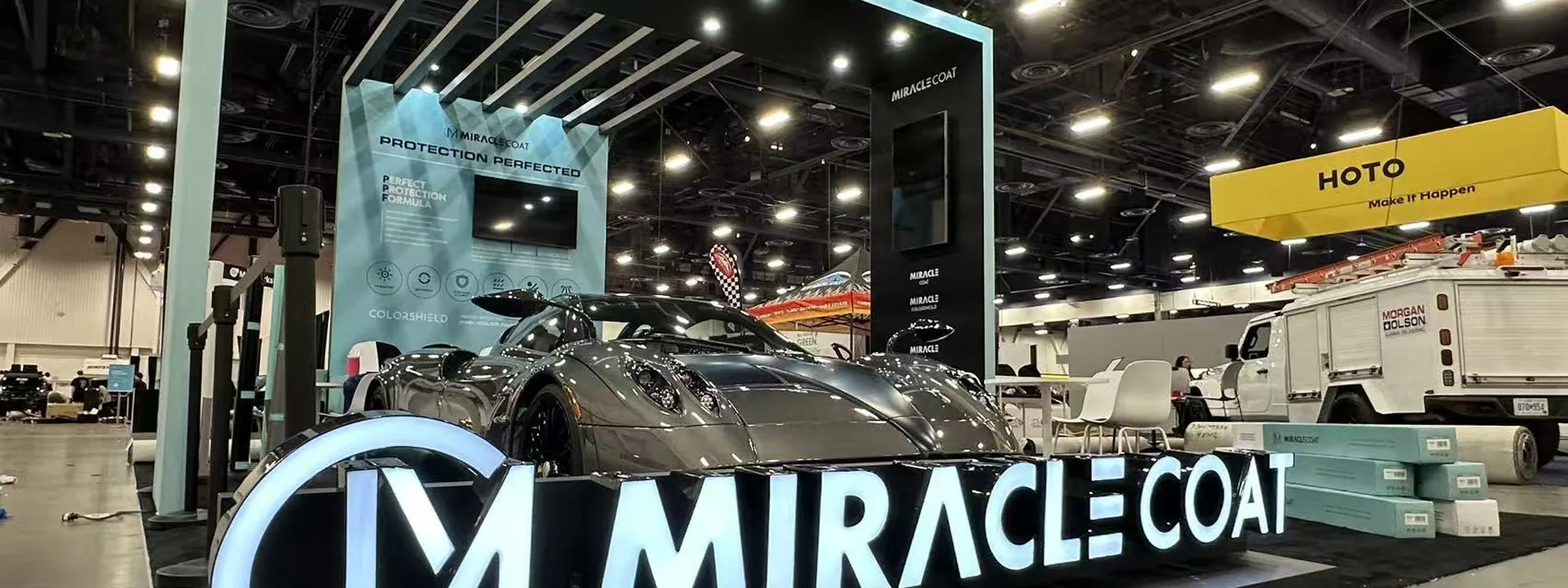 Automotive trade show booth with an illuminated frame, branded reception counter, car display, and meeting area.